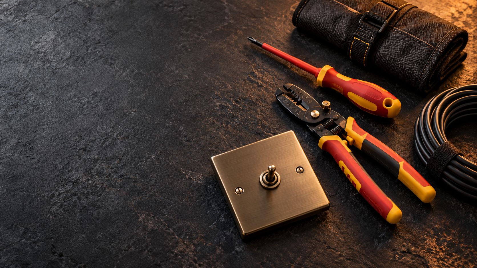 An insulated screwdriver, pliers and a bronze toggle switch on a dark slate surface